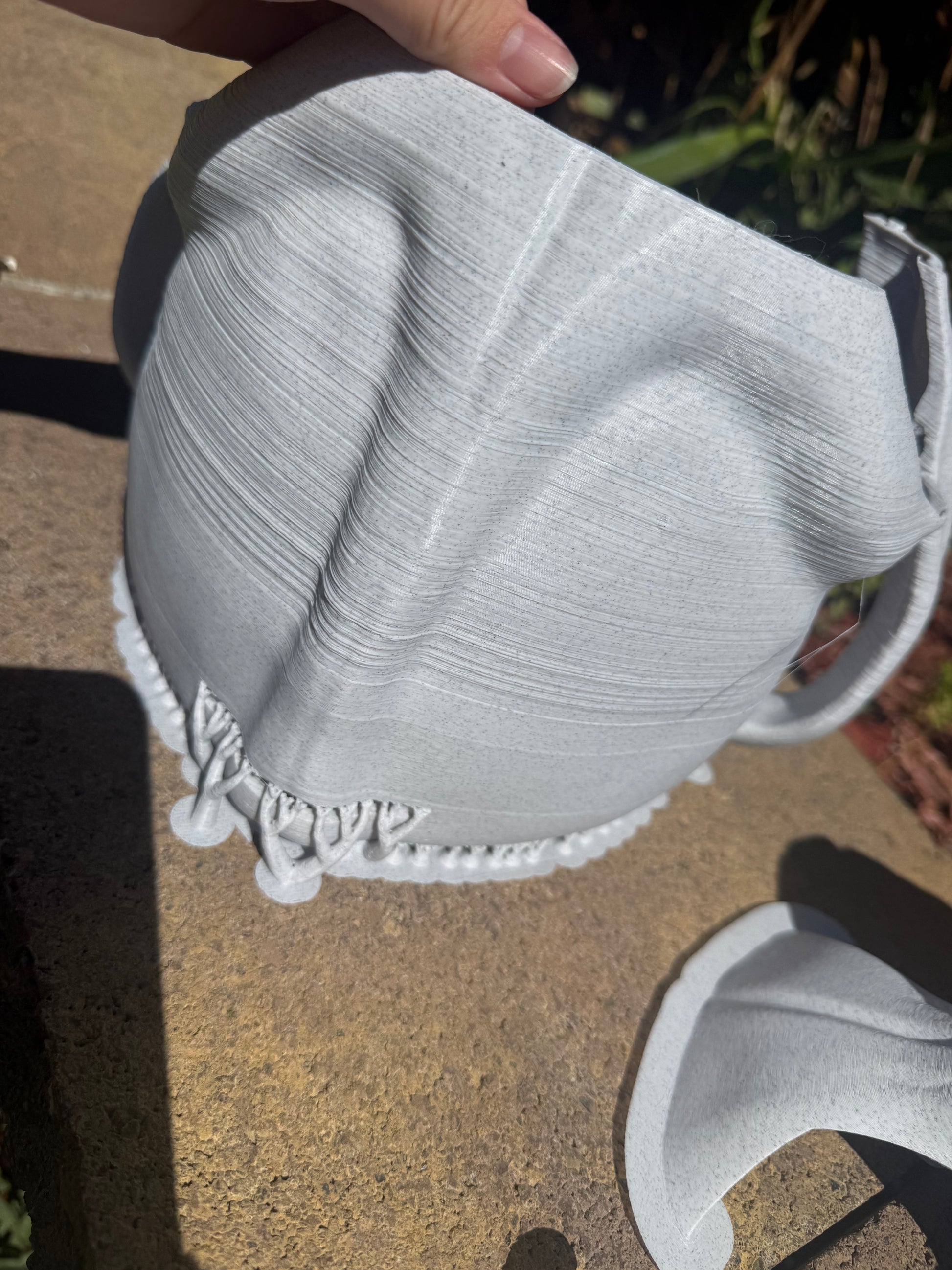 Half of A light gray 3D-printed k9 skull sculpture displayed outdoors on a concrete patio with plants in the background.